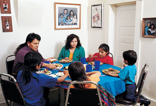 Native American family sitting down at a table to have a meal.