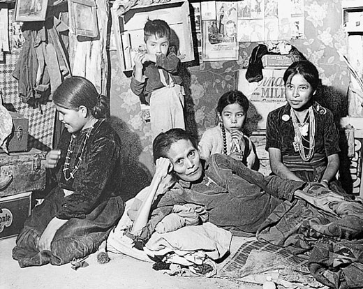 Four native American children and a native American woman sitting on the floor.