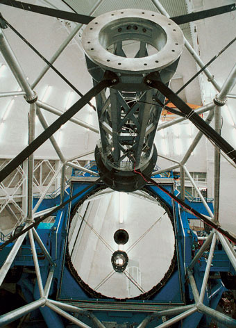 Large mirror sits on a framework underneath of a telescope tube. 