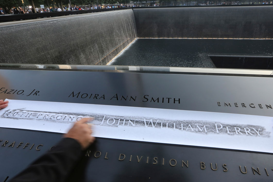 A hand tracing the name John William Perry onto paper at the 9 11 Memorial plaza. 