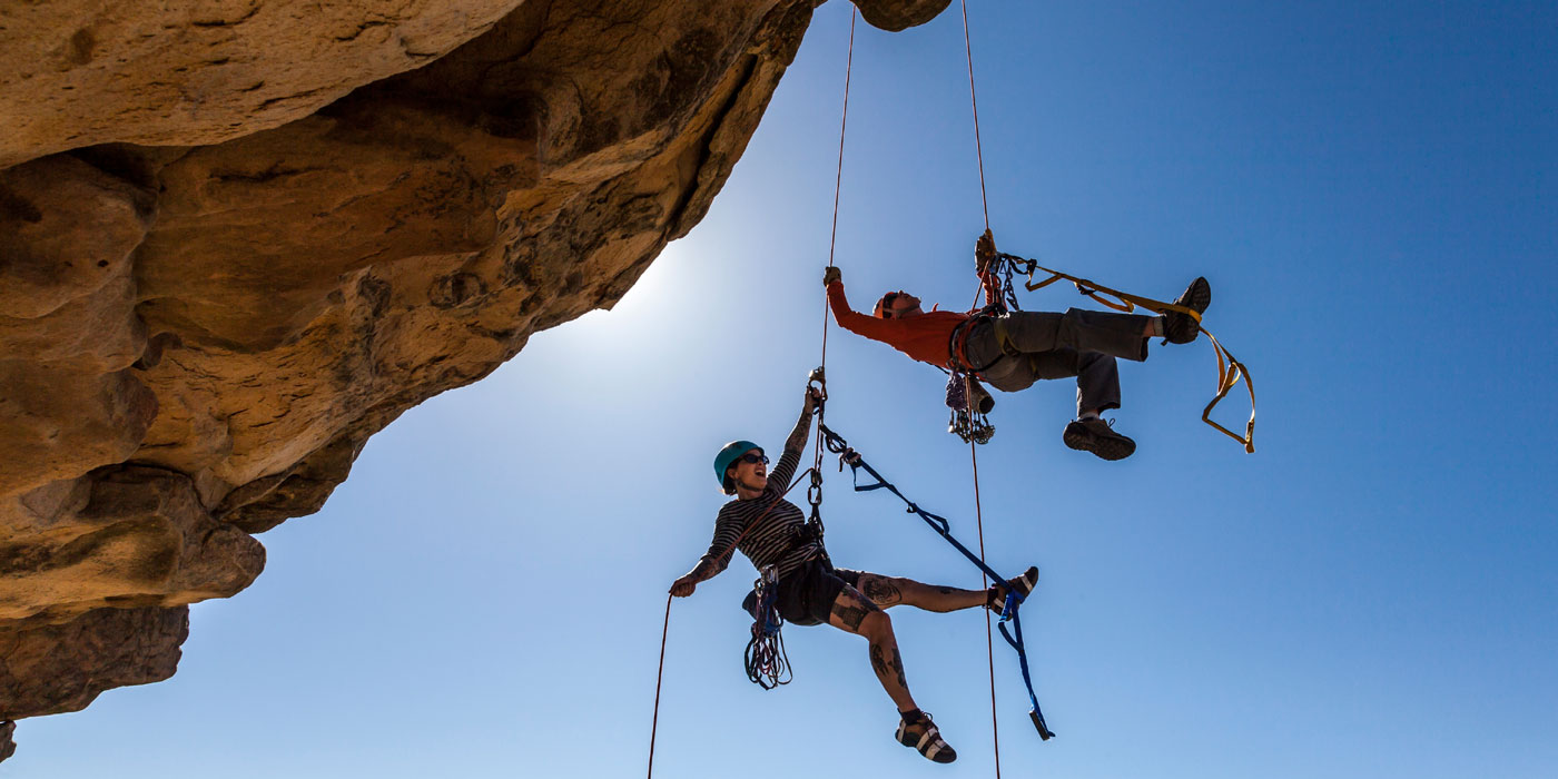 Two rock climbers hang from ropes attached to a rocky cliff.