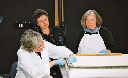Three ladies wearing gloves work to restore damage to the Declaration of Independence.