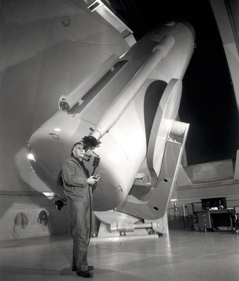 Edwin Hubble standing next to a large telescope. 