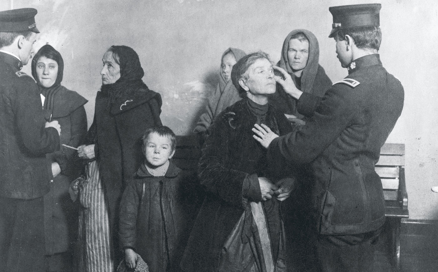 Black and white photograph shows immigrants going through the screening process at Ellis Island.