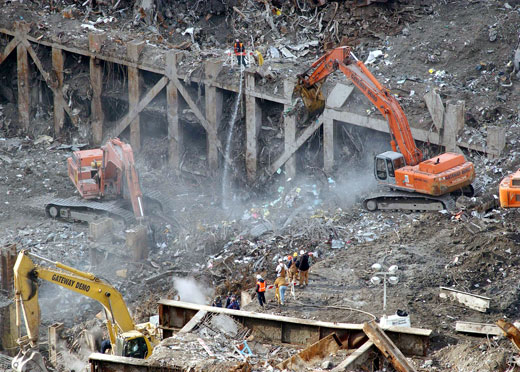 Workers and excavators clearing debris amid dust and smoke.