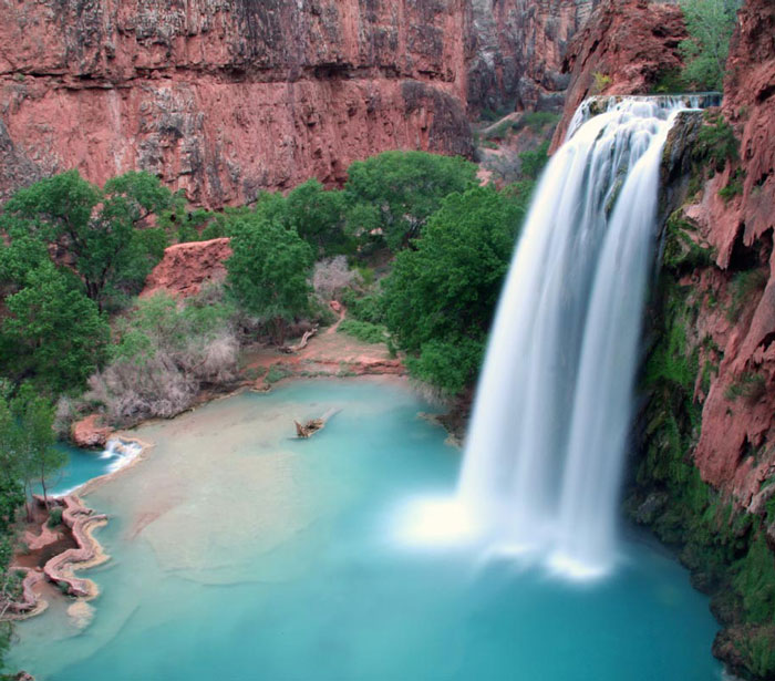 Majestic waterfall pours into a crystal lake that is between several tall rock faces.
