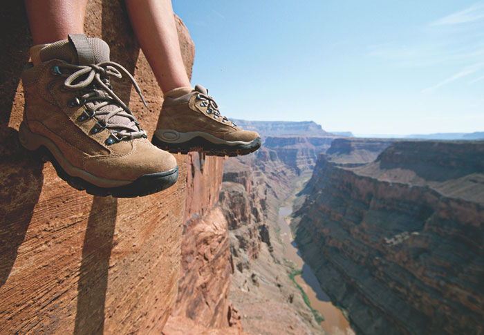 Person sits with their feet dangling over the side of a cliff with a view of a river below them.