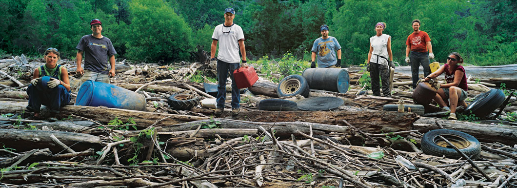 Group of people posing on a large pile of tree branches with garbage scattered around them.