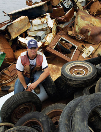 Man sitting on a pile of tires and trash collected from the banks of a river.