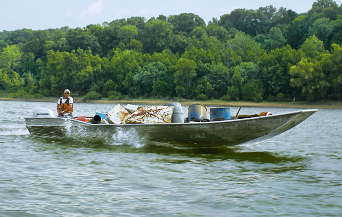 Man traveling down a river in a boat filled with trash.