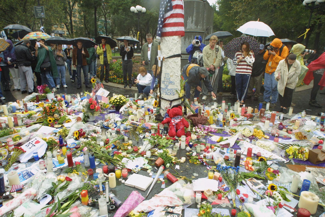 People gathered around a memorial of flowers, candles, and messages.