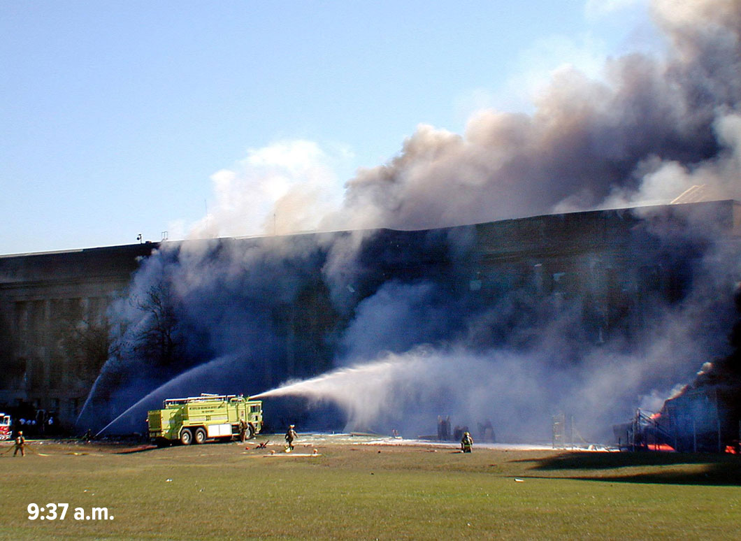 Fireman and a fire truck spraying water at a smoking Pentagon building, with a time stamp of 9:37 a.m.