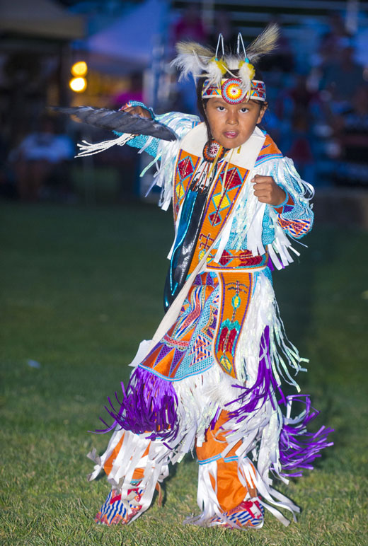Native American boy wearing traditional clothing, including feathers on his head.