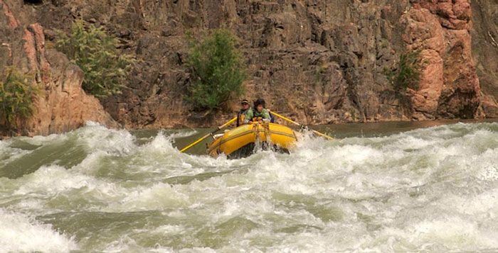 People in a rubber boat riding the rapids along a river. 