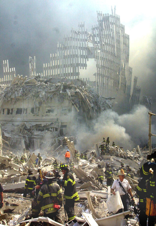 Several firefighters examining through ruins and smoke in front of the collapsed World Trade Center.