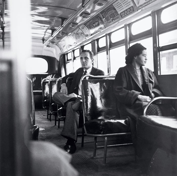 Rosa Parks riding on a bus with a white passenger sitting behind her.