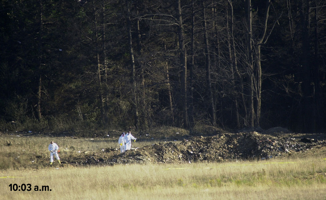 Three individuals investigating a debris area in a grassy field, with a time stamp of 10:03 a.m.