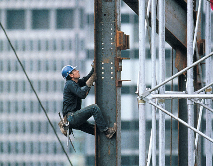 Native American construction worker climbs a beam of a new building.