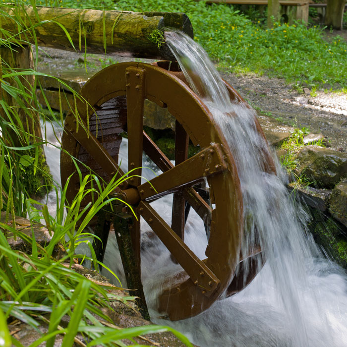  A paddle wheel being turned by water pouring over it from a pipe made of a hollowed log.