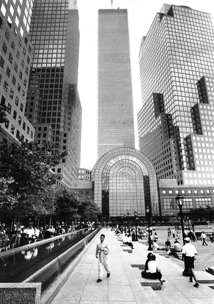 People sitting or walking in the area in front of the World Trade Center.