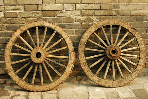 Wagon wheels rest against the side of a building.