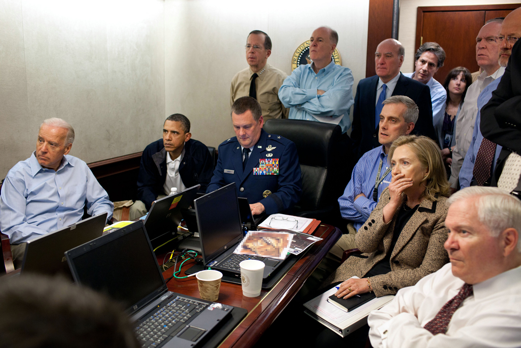 President Obama, Vice President Biden, and officials in the White House, sitting around a conference table watching a monitor.