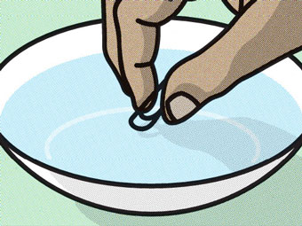 Person placing a paperclip on the surface of a bowl of water.