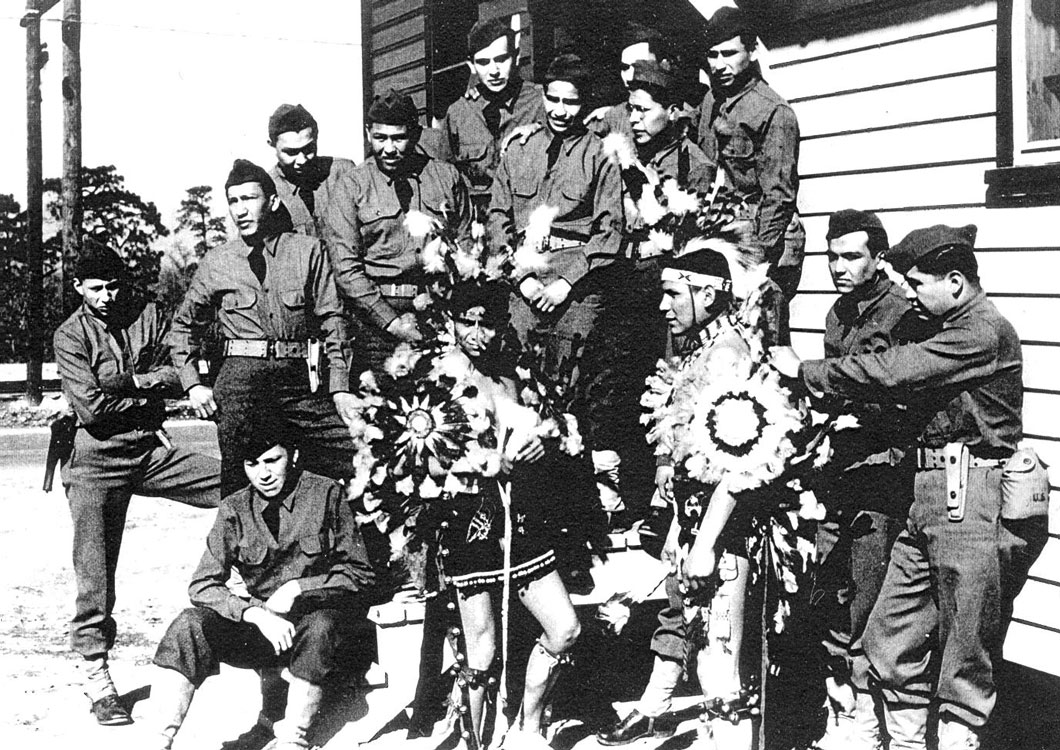 Group of Native American soliders, most in uniform, but one wearing traditional garb.