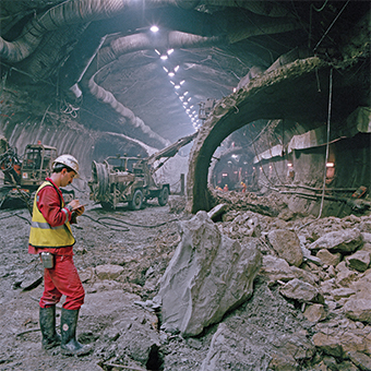 A construction worker standing near a pile of rocks as bull dozers work.