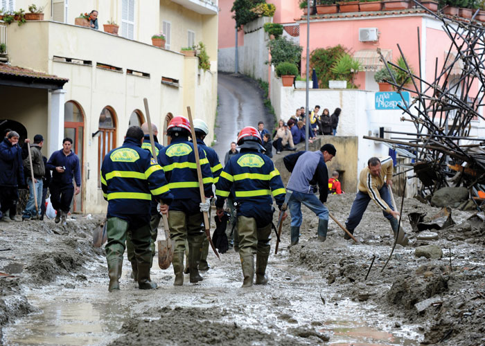 Workers walking though deep mud in the middle of a street as others dig through it. 