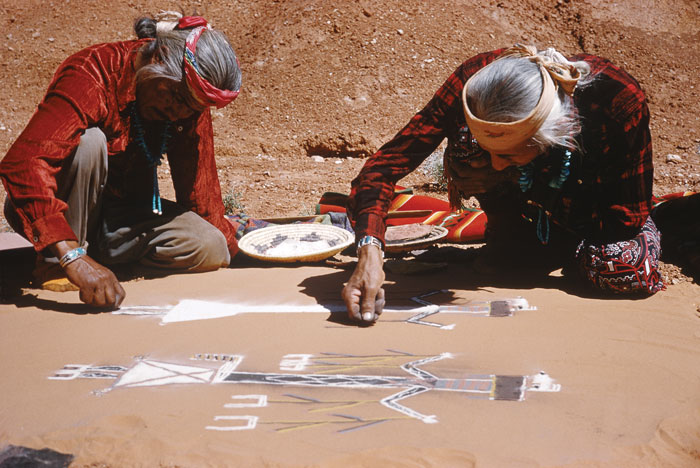 Two native people drawing images of birds and spirits on rocks.