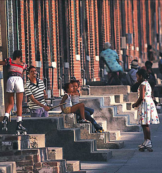 Adults and children sitting and playing outside homes on steps in the city.