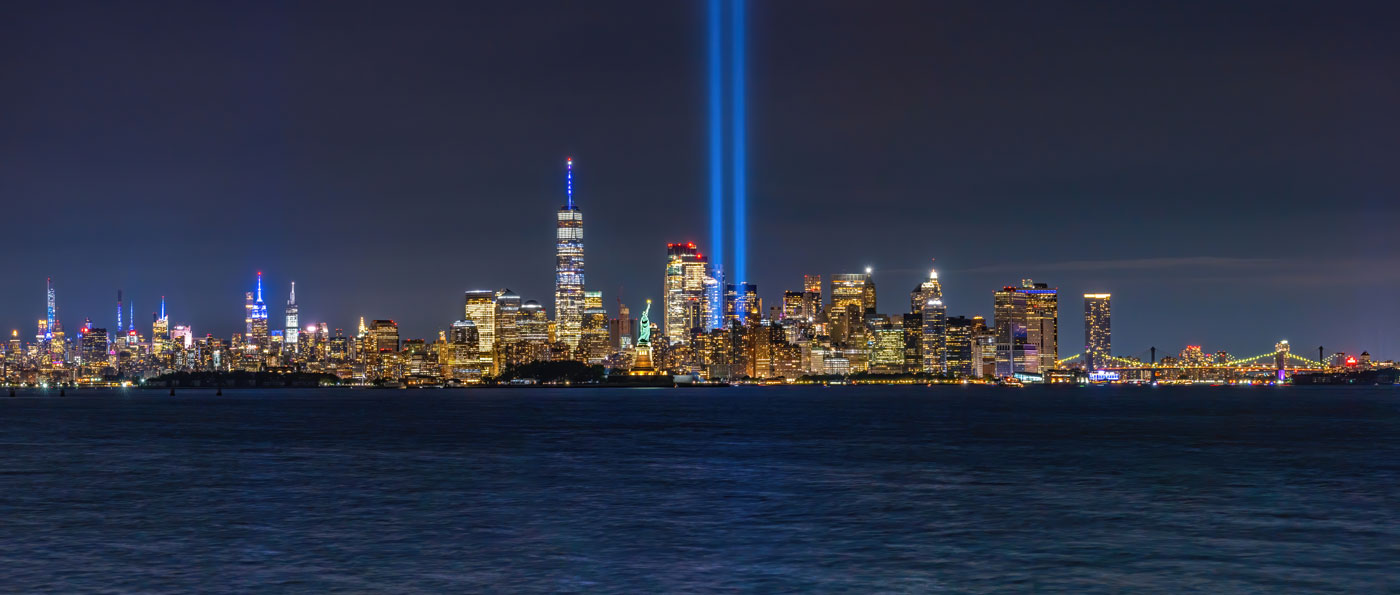 The New York City skyline at night with two bright lights beaming upward.