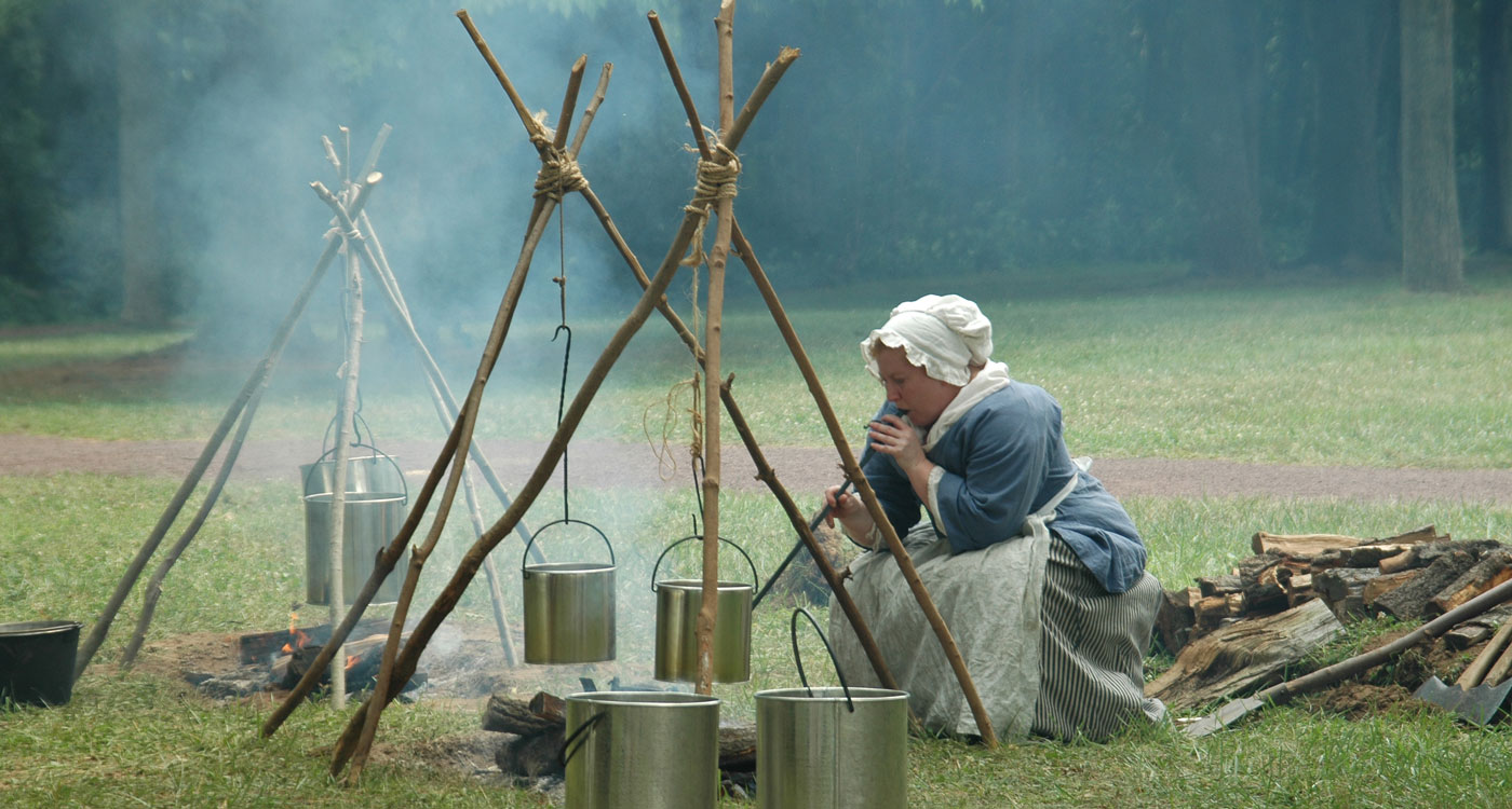 Colonial woman tending a fire at an army camp.